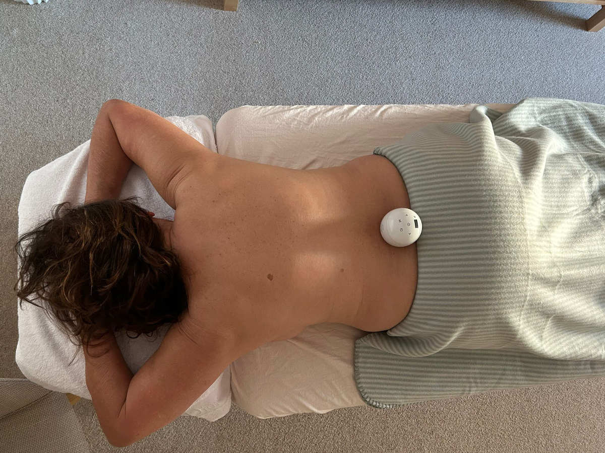 Massage mit Klangei: Eine entspannende Behandlung mit einer Klangschale in Ei-Form. Die Therapeutin führt das Klangei sanft über den Körper des entspannten Kunden auf der Massageliege.